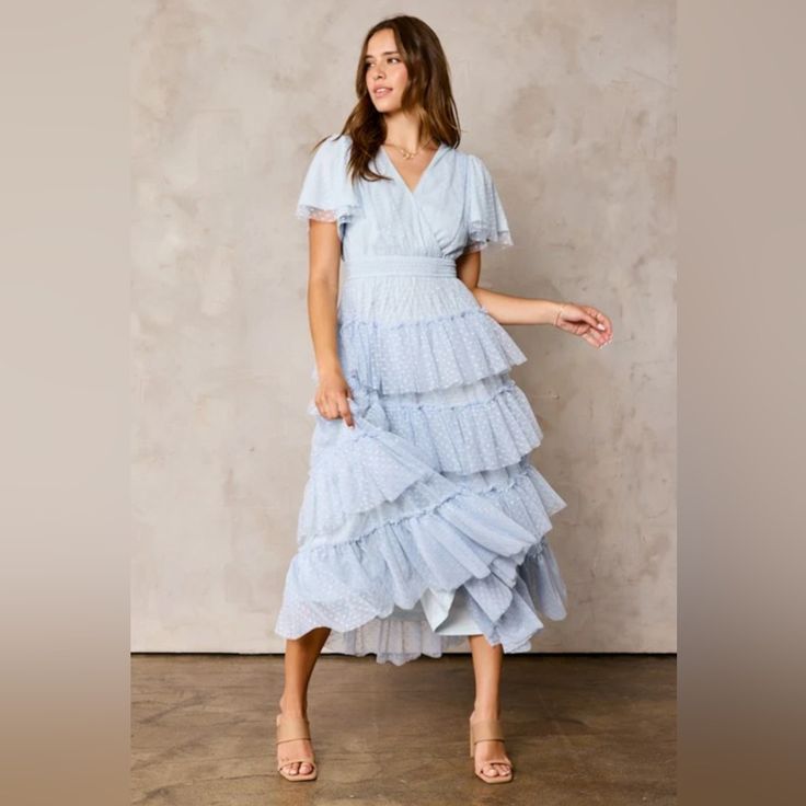 a woman wearing a blue tiered dress standing in front of a concrete wall with her hand on her hip