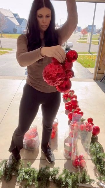 a woman standing in front of a christmas wreath with red balls and greenery on it