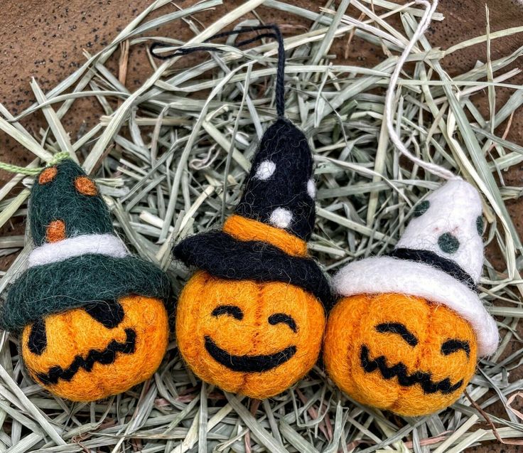 three knitted pumpkins sitting on top of hay with witches hats and brooms