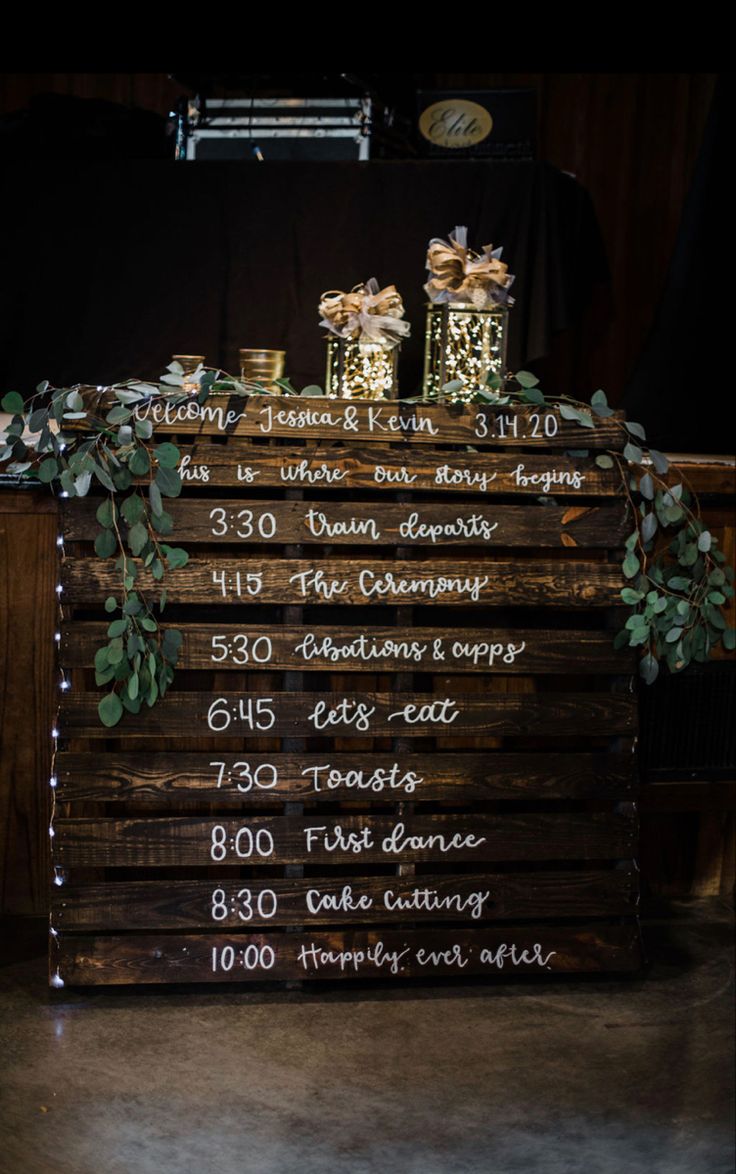 a wooden sign sitting on top of a table covered in flowers and greenery next to jars filled with candles