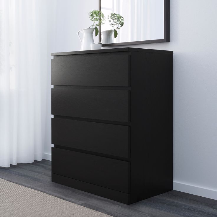 a black dresser with three drawers in front of a white wall and a mirror above it