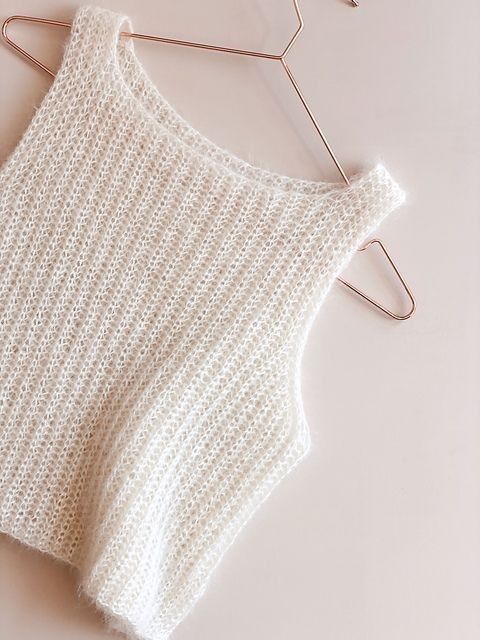 a white knitted sweater hanging on a clothes hanger next to a pair of scissors