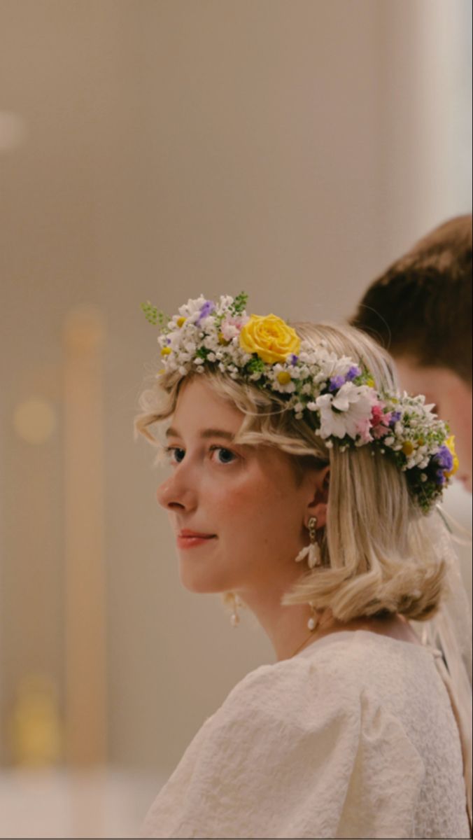 a woman with flowers in her hair wearing a white dress and standing next to a man