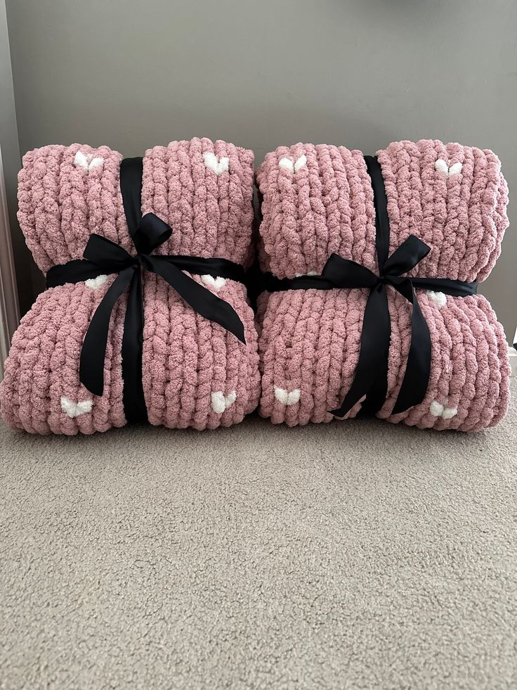 three pink crocheted blankets wrapped in black ribbon with white hearts on the front