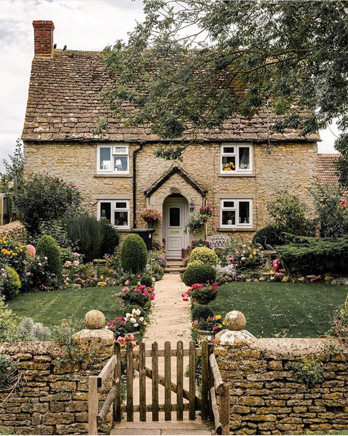 a stone house with flowers in the front yard and steps leading up to it's entrance