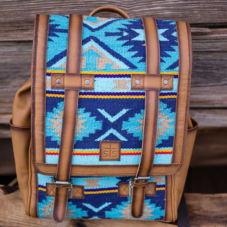 The Mojave Sky Knapsack by STS is designed for style and durability. It features a colorful Serape pattern and quality leather construction with a sky blue finish. This knapsack ensures a secure fit and lasting comfort. MULTICOLOR BLUE SERAPE WITH TAN/BROWN ENZME LEATHER ACCENTS GENUINE FULL GRAIN LEATHER STRAPS TOP FLAP CLOSURE BACKPACK STRAPS; TOP HANDLE 1 NTERIOR SCRUNCH POCKET PADDED LAPTOP SLOT CONCEAL CARRY HOLDER 12” W x 15”H x 6”D Blue Backpack Bag For Trip, Blue Travel Bag With Leather Backing, Outdoor Blue Leather Bag, Blue Backpack For Trips, Blue Leather Bag For Outdoor Use, Blue Backpack For Trip, Blue Leather Bag For Outdoor, Blue Leather Bag For Trip, Blue Leather Travel Backpack