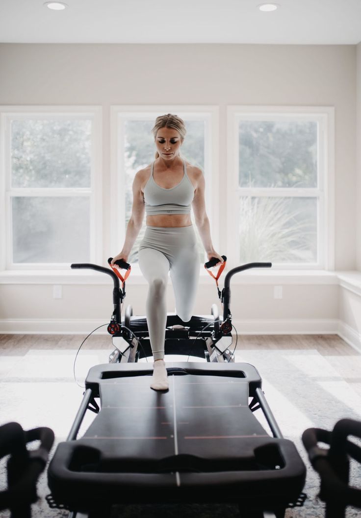 a woman standing on top of an exercise bike in a room with windows and flooring