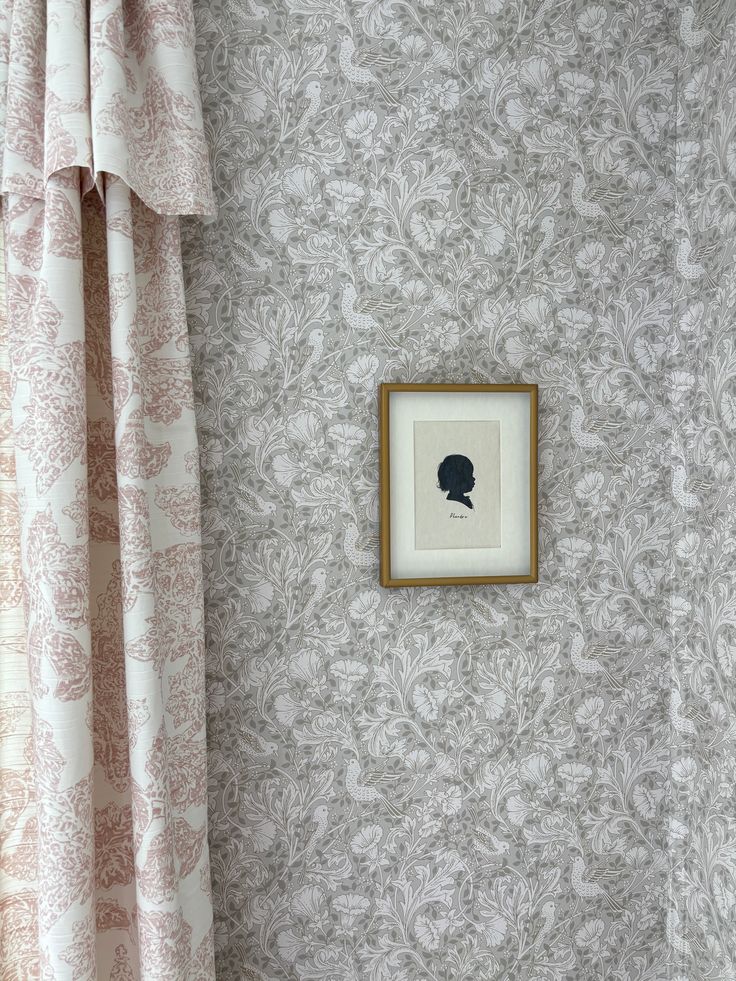 a small framed portrait hangs on the wall next to a window with drapes and curtains