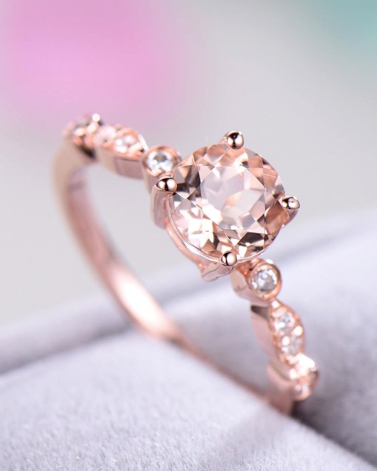 a ring with an oval shaped morganite surrounded by small white diamonds on a cushioned surface