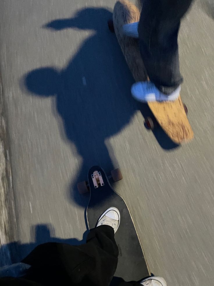 two skateboarders are riding their boards down the street in front of each other