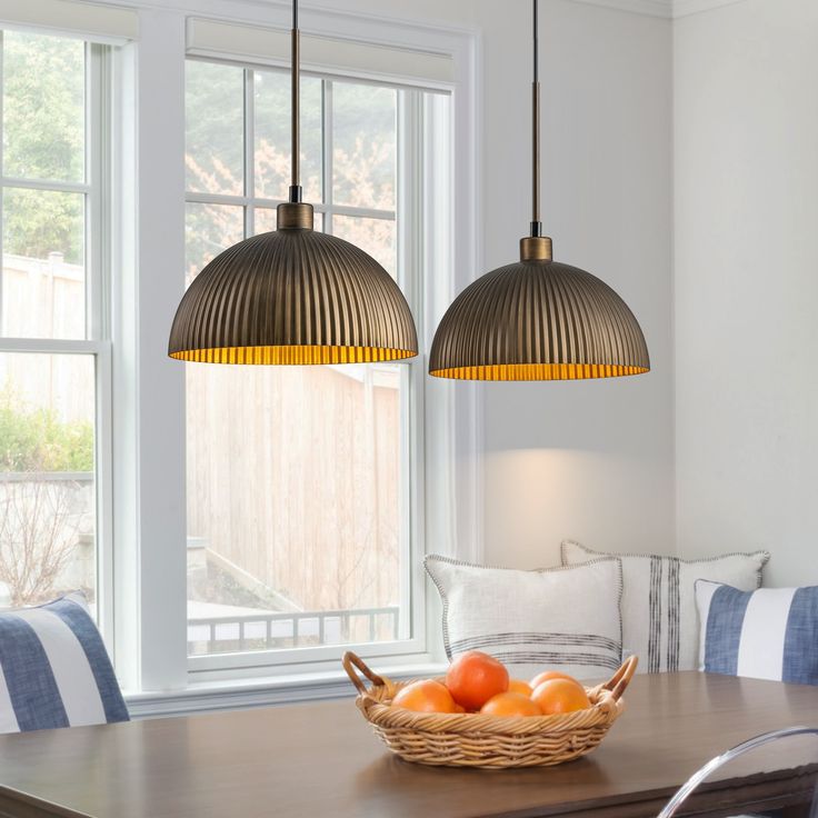 two hanging lights above a dining table with fruit in the basket on it and pillows