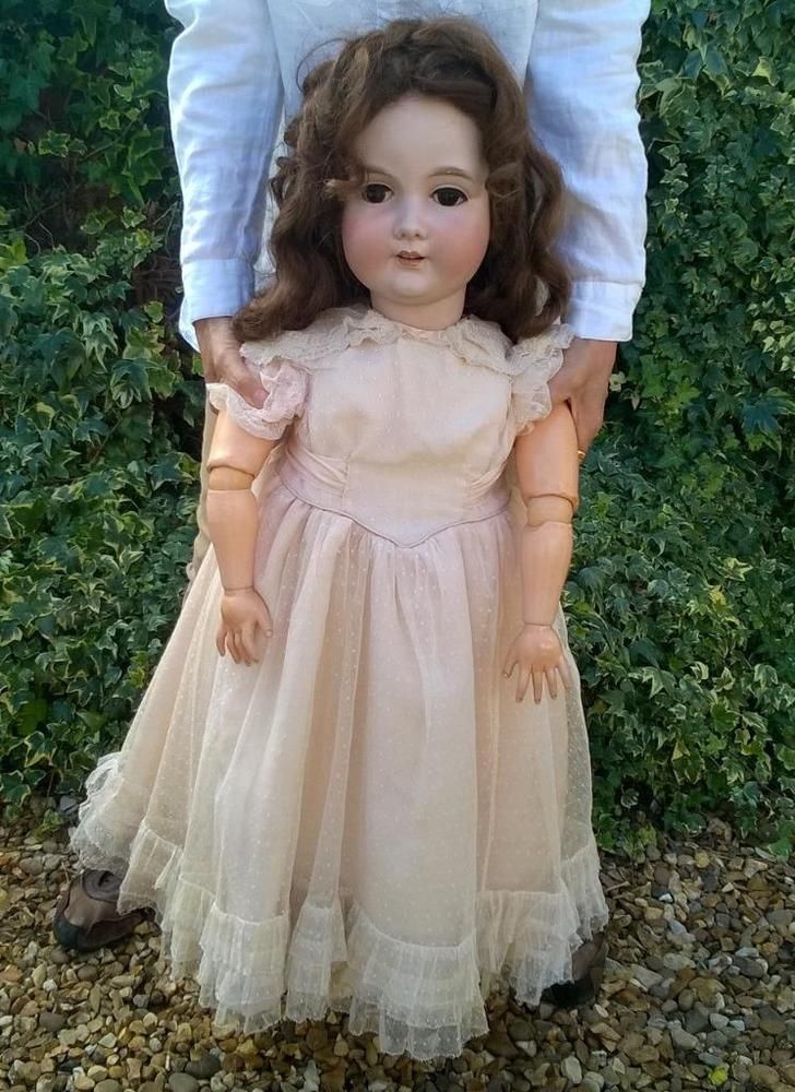 a doll is being held up by a man's hand in front of some bushes