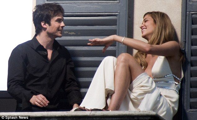 a man sitting next to a woman on top of a window sill near shutters