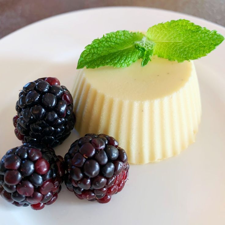 three berries on a white plate next to a piece of cheesecake and some mint leaves