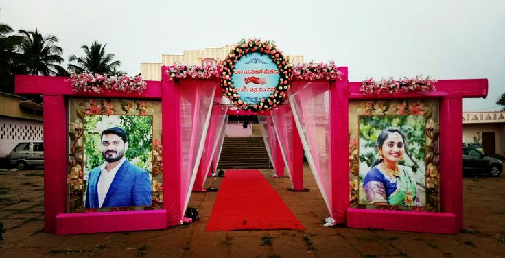 an entrance decorated with pictures and flowers on red carpeted walkway leading up to building