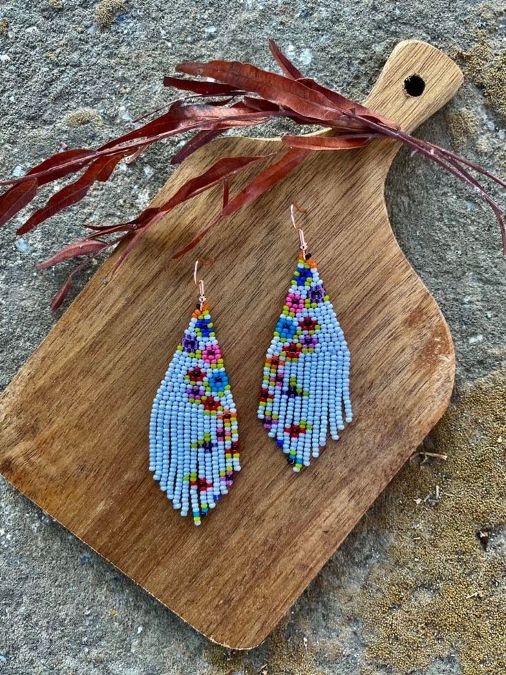 a pair of blue beaded earrings sitting on top of a wooden board next to some dry grass