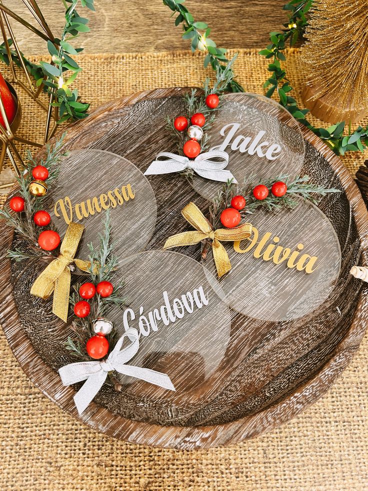 three personalized christmas ornaments on a wooden platter with red berries and greenery