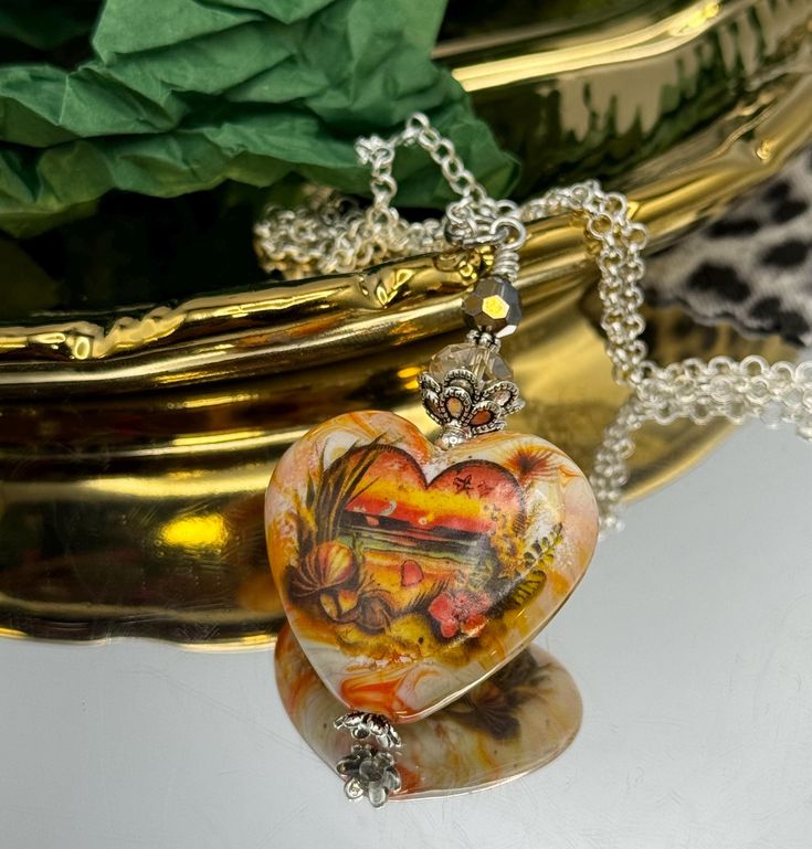 Embrace the beauty of a tropical sunset with this stunning heart-shaped pendant necklace. The intricately detailed pendant features a vivid beach scene with warm oranges, yellows, and earthy tones, capturing the serene moment of the sun setting over the horizon. Accented by sparkling beads and a delicate silver-tone chain, this necklace is a perfect blend of elegance and nature-inspired artistry. Ideal for beach lovers, travelers, or anyone looking to add a touch of warmth and color to their jewelry collection. **Key Features - **Design Heart-shaped pendant with a tropical beach sunset scene - **Materials lampwork glass, crystal beads, silver-tone metal  - **Color Multicolored with orange, yellow, and earthy tones - **Chain Length Approximately 22" inches with a secure lobster clasp - **Pe Midwestern Style, Orange Jewelry, Tropical Sunset, Heart Shaped Pendant Necklace, Heart Shaped Pendant, Sun Setting, Handmade Heart, Beach Scene, Heart Shape Pendant