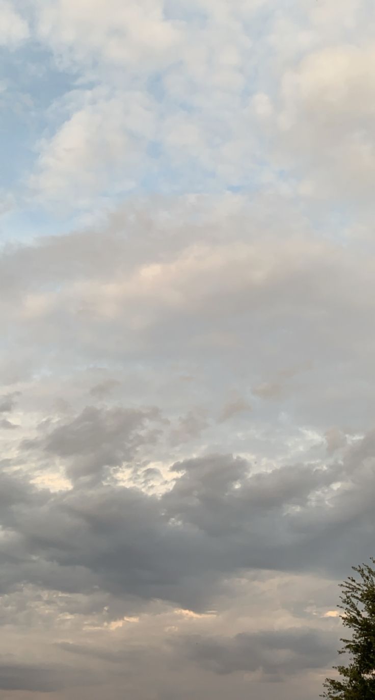 an airplane is flying high in the sky with some clouds above it and trees below