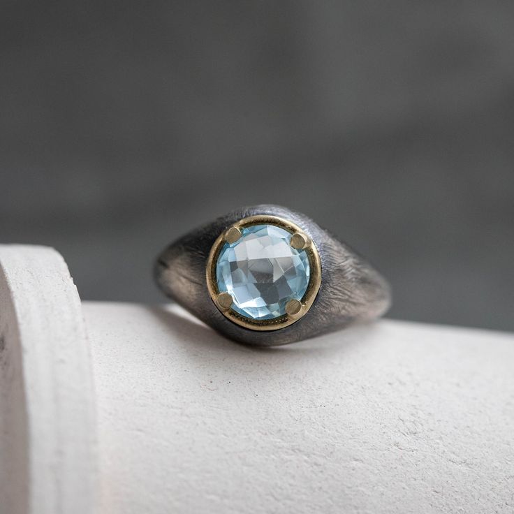 "A brutalist sterling silver ring for men and women with a genuine blue topaz gemstone in a 14K solid yellow gold bezel. This unisex rustic dome ring is 100% hand carved and it is an excellent choice for a Father's Day gift for him. D E T A I L S * Metal: High Quality Sterling Silver 925, 14K Yellow Gold * Finish: Black Oxidized * Width: 13 mm * Blue topaz 8mm, briolette cut, 2.7ct, Natural Gemstone 100% nickel free. Delivered in an elegant gift package. S H I P P I N G All orders are shipped vi Handmade Unique Blue Topaz Ring, Unique Handmade Silver Topaz Ring, Mens Blue Topaz Rings, Handmade Blue Topaz Ring In Sterling Silver, Blue Topaz Gemstone Signet Ring Gift, Luxury Silver Men's Ring With Blue Topaz, Birthday Ring, Domed Ring, Topaz Gemstone