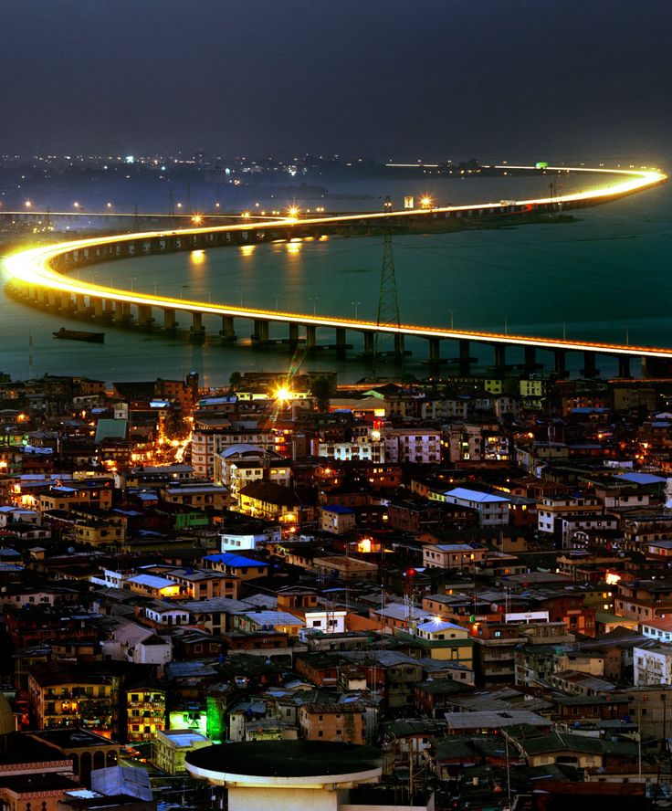 an aerial view of a city at night with lights on the buildings and water in the background