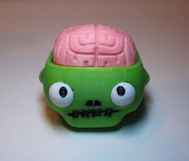 a green and pink toy skull with large eyes on it's head sitting on a white surface