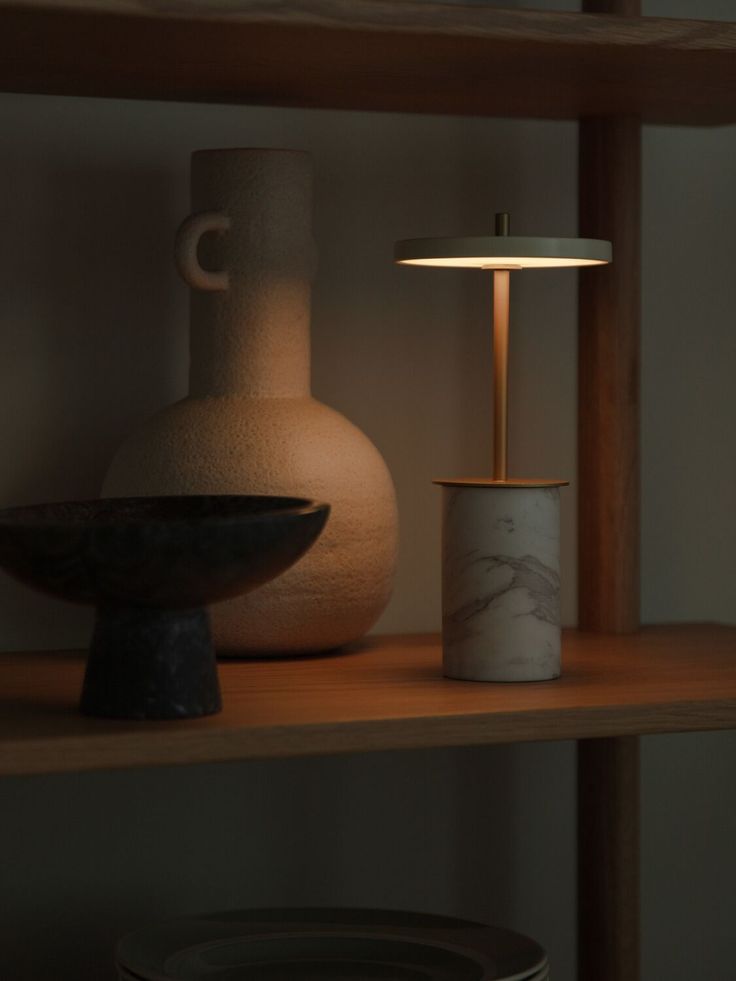 a table lamp sitting on top of a wooden shelf next to a vase and bowl