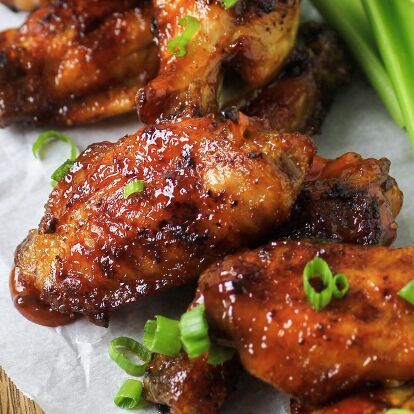 chicken wings with sauce and green onions on a piece of wax paper next to some scallions