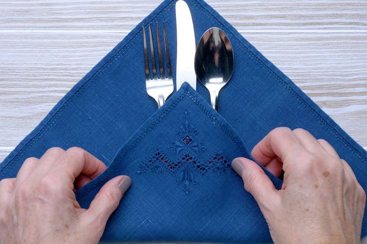 two hands are holding silverware on top of a blue napkin that is folded in the shape of a cross