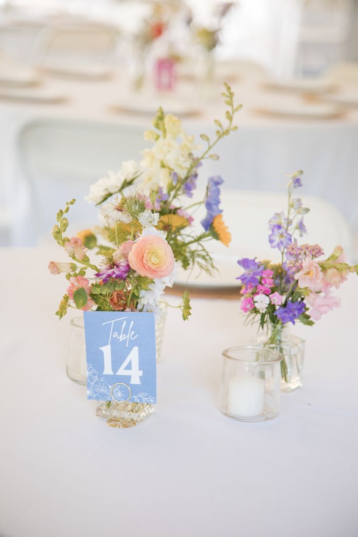 two vases filled with flowers on top of a white table cloth covered tablecloth