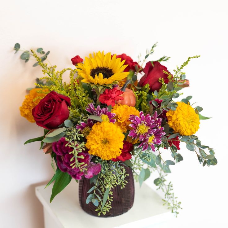 a vase filled with lots of colorful flowers on top of a white table next to a wall