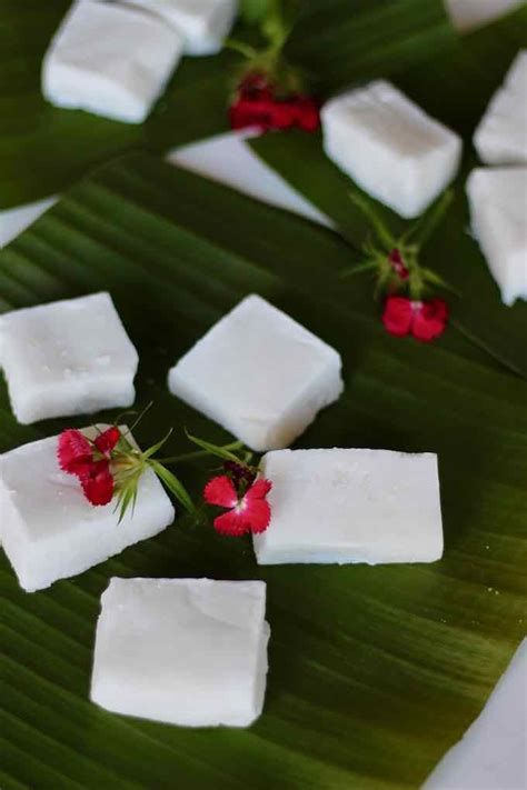 several pieces of white food sitting on top of a banana leaf with red flowers in the middle