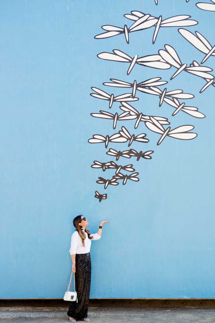 a woman standing in front of a blue wall holding a white bag and pointing at something