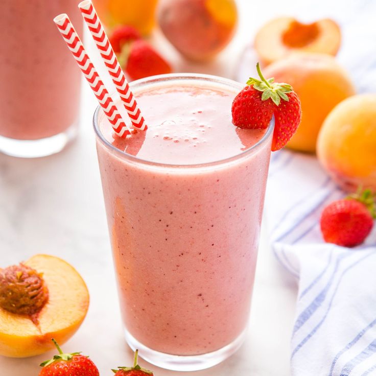 there is a smoothie with strawberries on the table next to peaches and oranges