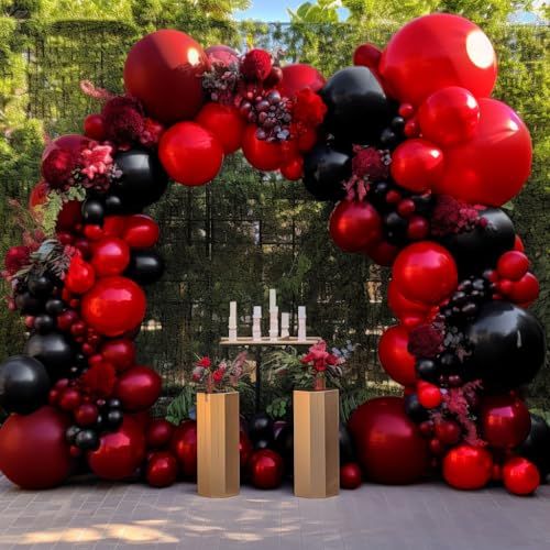 a large red and black balloon arch is decorated with flowers, candles, and balloons