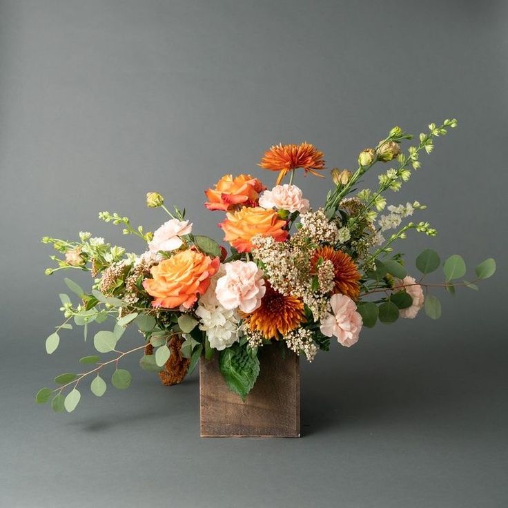 an arrangement of flowers in a wooden vase on a gray background with greenery and leaves