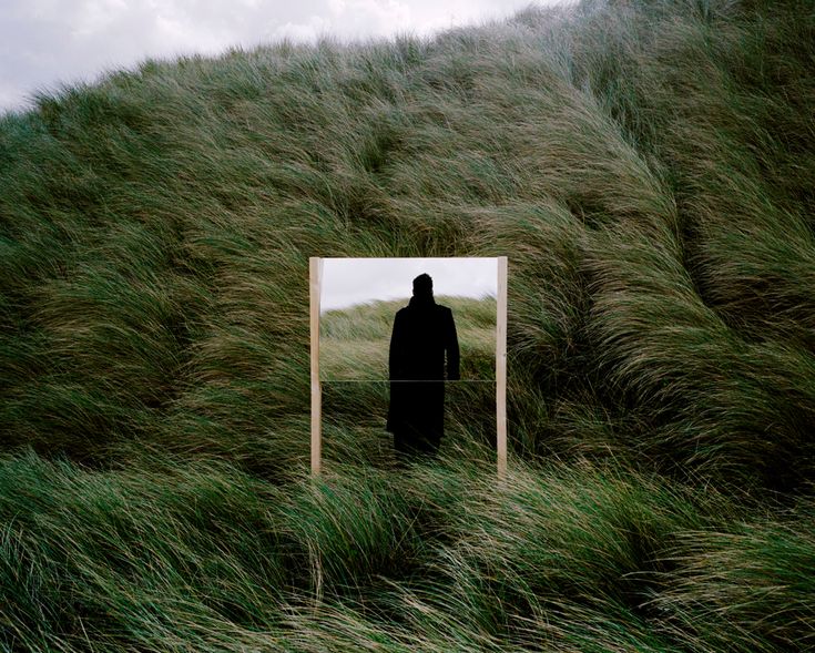 a man standing in front of a mirror on top of a grass covered hill,