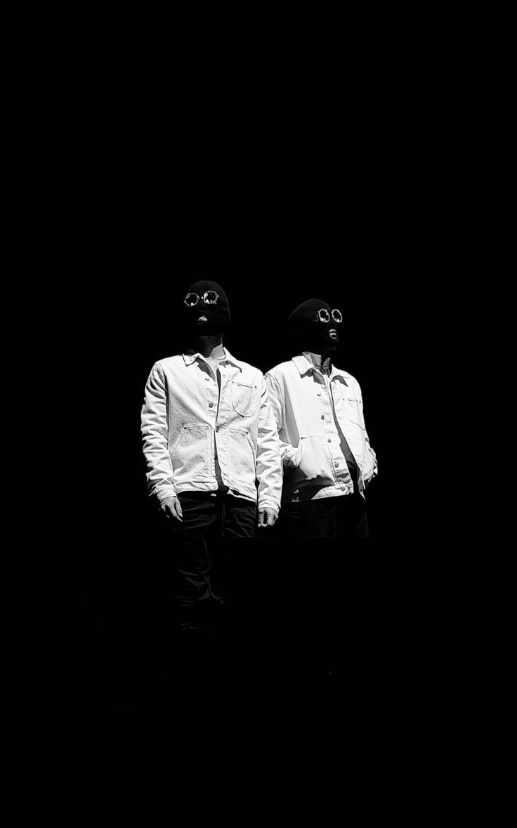 two men standing next to each other in front of a black background wearing goggles