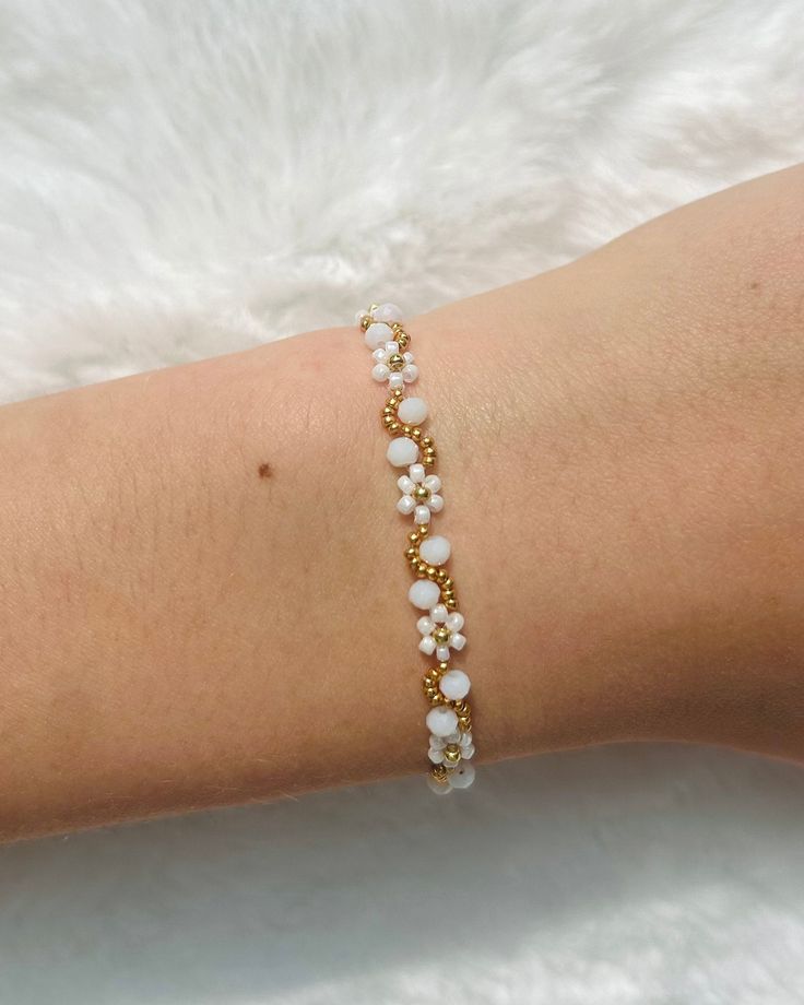 a woman's arm wearing a gold and white beaded bracelet with pearls on it