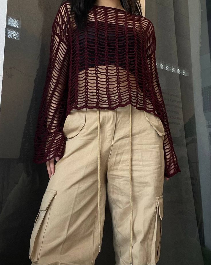 a woman standing in front of a window wearing beige pants and a maroon top with crochet