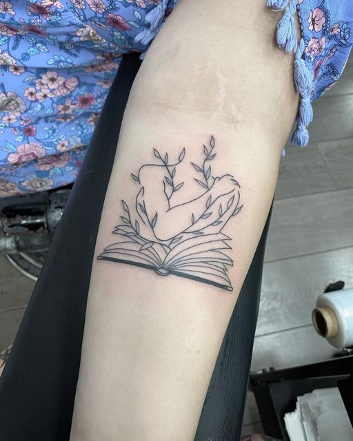 a woman with a tattoo on her arm holding an open book and flowers in the shape of a heart