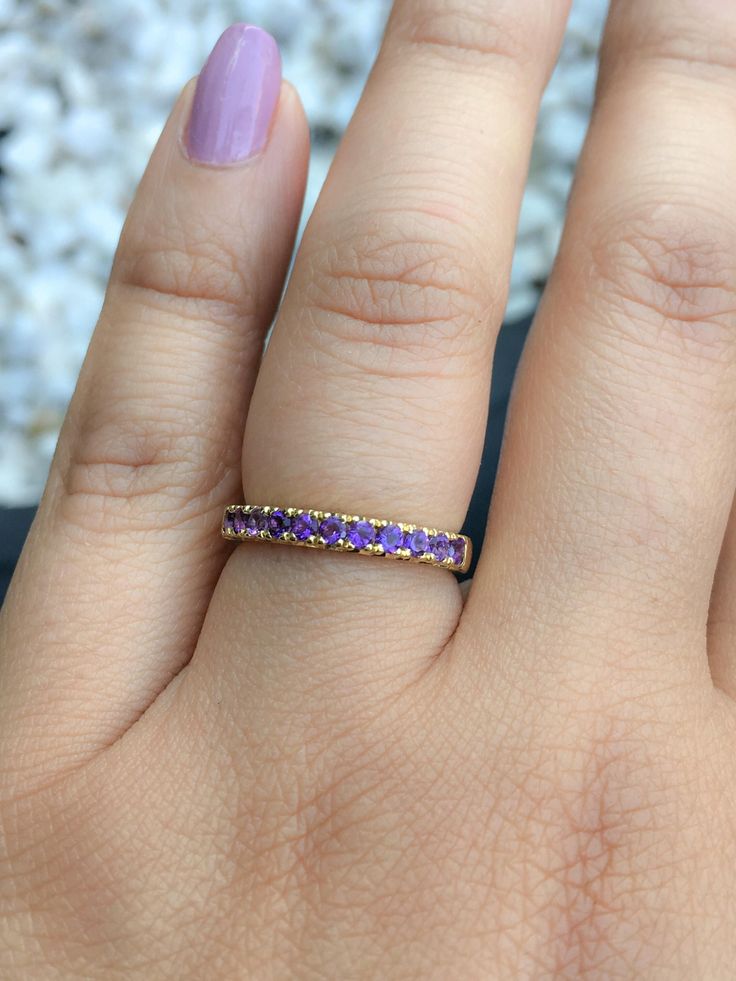 a woman's hand with a gold band and purple stones on the middle finger