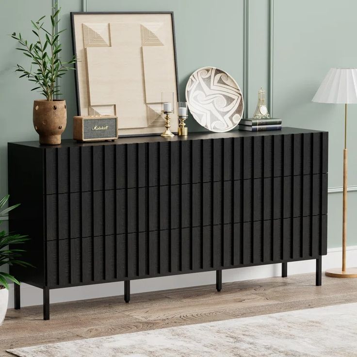 a black dresser sitting on top of a wooden floor next to a lamp and potted plant