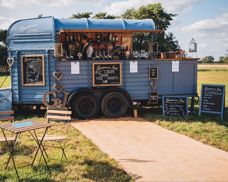 a food truck is parked in the grass with tables and chairs around it, along with chalkboard menus