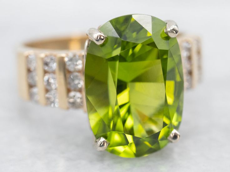 This stunning modern ring is an example of a classic simple four-prong mounting with glimmering channel diamond set sides, but what really sets this ring apart is the stone! The middle is amazing and is a rare stone; a super fine quality large peridot with some of the best color saturation and a deep entrancing green color that ranges from a deep grass green to light bright lemon-lime flickers in the light! Simply stunning!Metal: 14K Yellow Gold Gem: Peridot 8.97 Carats Gem Measurements: 15.4 x 10.8 mm, Oval Accents: 18 Diamonds totaling .50 Carats, H-J in Color, SI in Clarity Ring Size: 10.25Marks: "14K 3d" Stamped on the inside band Gold Peridot Ring, Right Hand Ring, Diamond Cocktail Ring, White Gold Solitaire, Gold Solitaire Ring, Engagement Ring Diamond Cut, Rare Stone, Right Hand Rings, August Birthstone