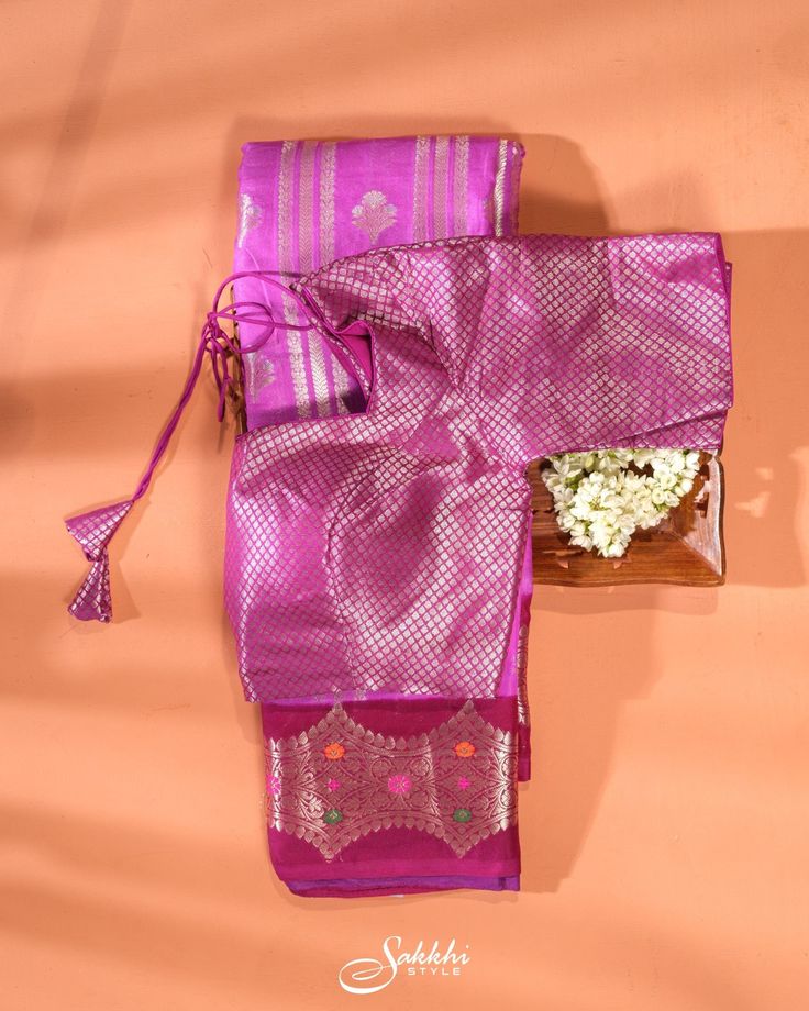 A Banarasi art silk saree, featuring a harmonious blend of mulberry pink and maroon hues. The baby blue section is embellished with vertical zari stripes alternated by zari buttis throughout, adding a distinct accent to the overall look. The saree is further enhanced by a contrasting border adorned with zari floral work, highlighted with multicolored thread embroidery. The ensemble includes a pre-stitched readymade blouse in matching colors with the border. The saree's smooth and luxurious feel, coupled with the elbow-sleeved blouse, ensures a perfect fit for a sophisticated appearance. Banarasi art silk saree for special occasions. Crafted from the premium quality fabric. Designed with zari stripes and buttis throughout. Supplied with a readymade blouse in matching with border hue. The bl Purple Art Silk Pre-draped Saree With Self Design, Traditional Purple Pre-draped Saree For Navratri, Purple Self-design Pre-draped Saree For Puja, Traditional Purple Pre-draped Saree For Puja, Purple Pre-draped Saree For Puja, Pink Raw Silk Pre-draped Saree For Puja, Purple Raw Silk Pre-draped Saree With Cutdana, Purple Art Silk Pre-draped Saree For Navratri, Pink Pre-draped Saree With Unstitched Blouse For Festivals