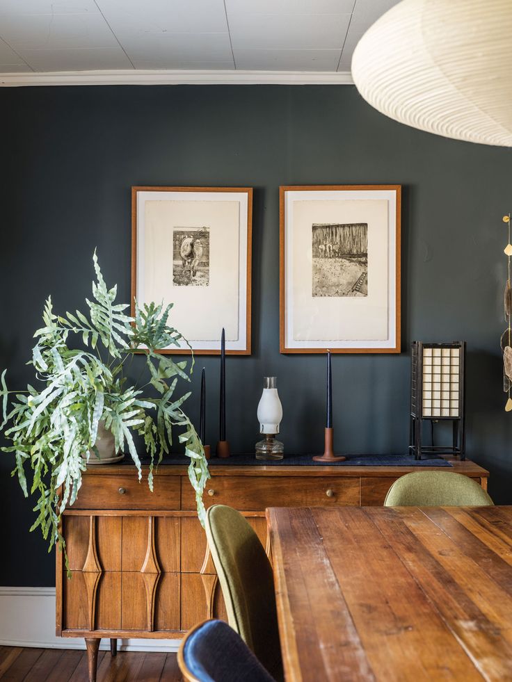 two framed pictures hang on the wall above a wooden table with chairs and a potted plant