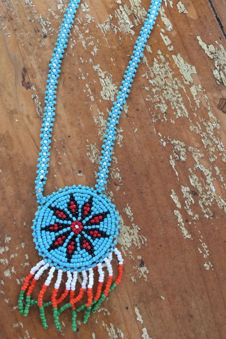 a blue beaded necklace with an orange, white and red flower on it sitting on a wooden surface