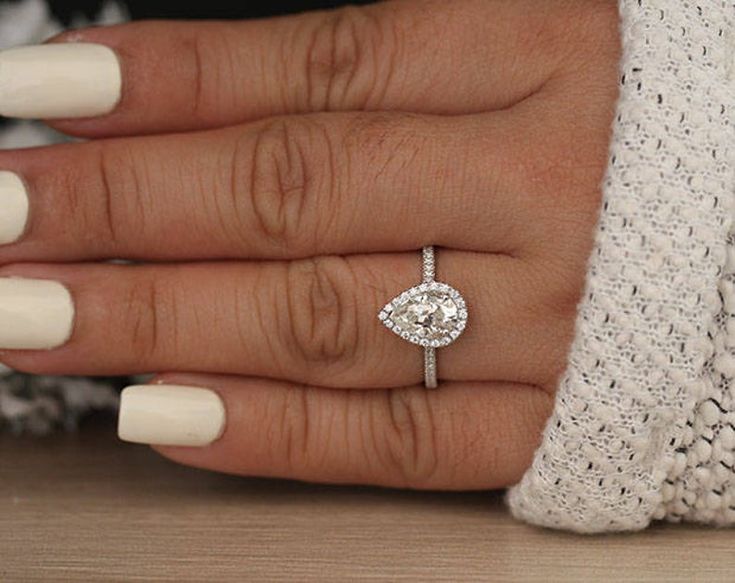 a woman's hand with a diamond ring on her finger and white manicured nails