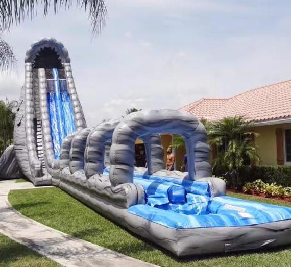 an inflatable water slide is on the lawn next to a house and palm trees